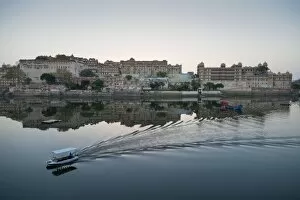 A water taxi passing the City Palace reflected in the still dawn waters of Lake Pichola