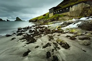 A waterfall cascading over the black sand beach of Bour into the Sorvagsfjorour