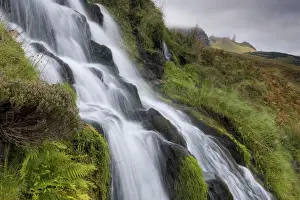 Portree Prints: Waterfall cascading down grassy slope with Old Man of Storr in background