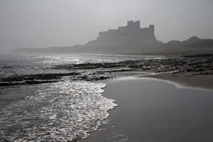 Northumberland Prints: Waves breaking at Bamburgh Beach looking towards Bamburgh Castle on a misty morning
