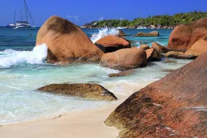 Relax Prints: Waves crash against rocky shore at Anse Georgette on Praslin island with boats in the background