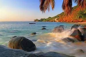 Retreat Prints: Waves crashing against rocks on a beach with palm trees at sunset in Seychelles