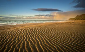 Rippled Gallery: Wind-swept sandy beaches of the Kalalau Valley at sunset with a partial rainbow in