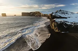 Black Sand Prints: Winter view towards snow covered headland at Dyrholaey bathed in evening sunlight