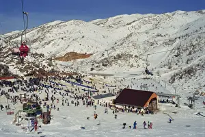 Skiers Prints: Woman on chairlift above crowds of skiers and tourists at the Neve Ativ Ski Resort on Mount Hermon
