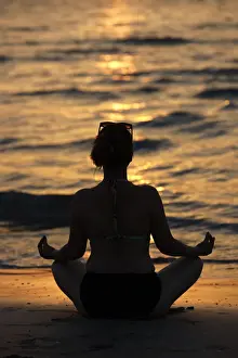 Woman practising yoga meditation on beach at sunset as concept for silence and relaxation
