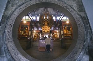 A woman praying in front of an arched entrance at West Garden Buddhist Temple