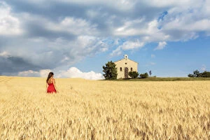 Contemplation Gallery: Woman in red dress admiring Notre-Dame-de-Sante chapel in a wheat field, Entrevennes