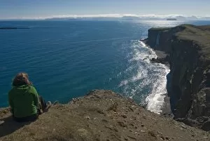 Woman sitting above the steep coast with cliffs, Vatnsnes Peninsula, Iceland