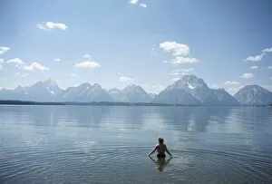 Woman wades in lake with Tetons in distance, Grand Teton National Park