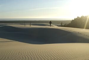 Woman walking barefoot on sand dunes torwards the Pacific Ocean, Southern Oregon