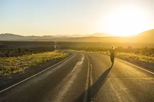 Caucasian Ethnicity Prints: Woman walking down a long winding road at sunset in eastern Nevada