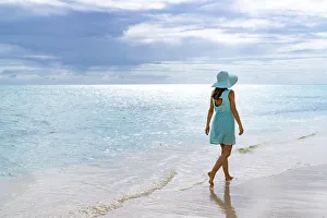 Mid Adults Prints: Woman walking on a white sand beach under the cloudy sky at sunset