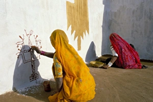 Jaisalmer Prints: Women painting design on a wall in a village near Jaisalmer