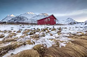 Winter Scene Prints: Wood hut framed by rocks covered with grass and ice with snowy peaks in the background