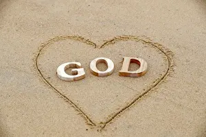 Heart Shape Prints: Wooden letters forming the word GOD with heart on a background of beach sand