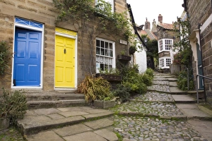 Yellow and blue doors on houses in The Opening, a narrow stepped cobbled alley on steep hill in Old Bay part of the fishing village, Robin Hoods Bay, Yorkshire, England, United