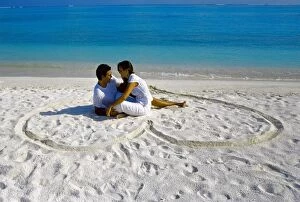 Images Dated 24th September 2009: Young couple on beach sitting in a heart shaped imprint on the sand, Maldives