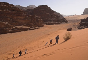 Wadi Rum Prints: Young people climbing a typical red sand dune with