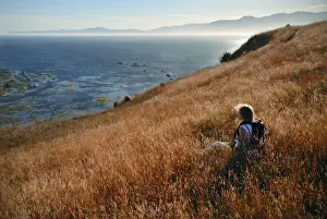 20 25 Prints: A young woman hiker rests in a wild grass field on the coast of New Zealand