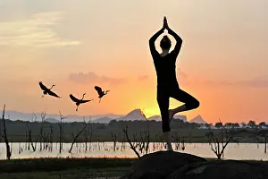 Meditation Prints: Young woman practising yoga posture by the Senanayake Samudraya Lake at sunset