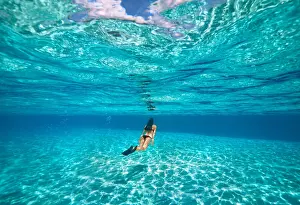 Adults Prints: A young woman swimming underwater in clear blue shallow lagoon with a sandy bottom