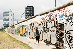 Graffiti Prints: Young woman walking past graffiti on former Berlin Wall, East Side Gallery, Muhlenstrasse