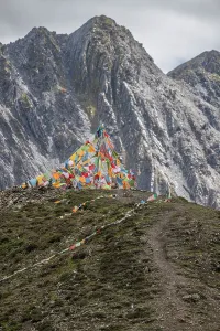Trekking Prints: Zimei mountain pass shows prayer flags on a rugged path under dramatic clouds in Sichuan